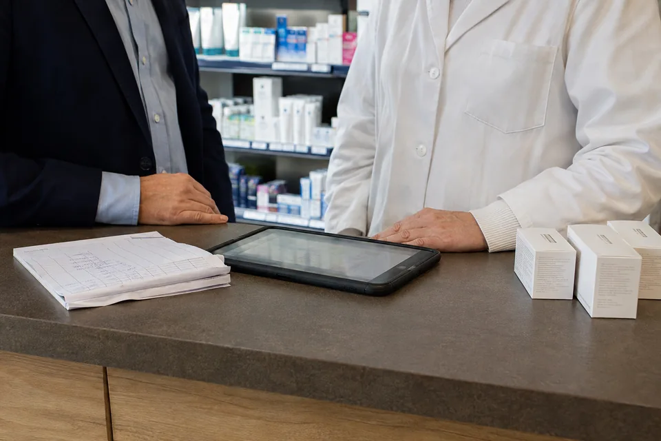 A tablet, a paper order form and skincare products on a pharmacy counter.