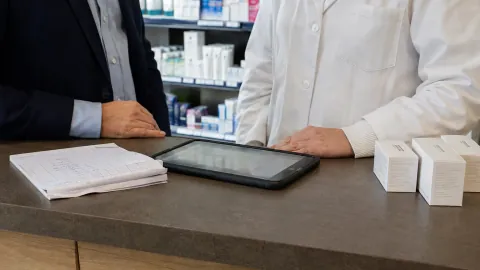 Une tablette, un bon papier et des produits de soin sur un comptoir de pharmacie.