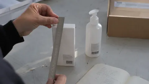 Hands measure a product box with a metal ruler on a packing table.
