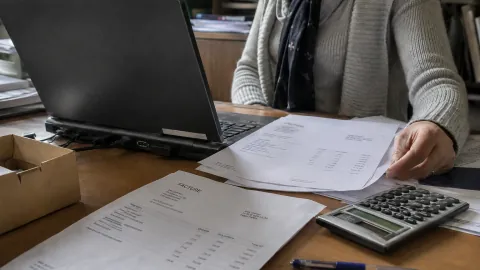 Invoicing paperwork, a calculator and a computer on a sales administration desk.