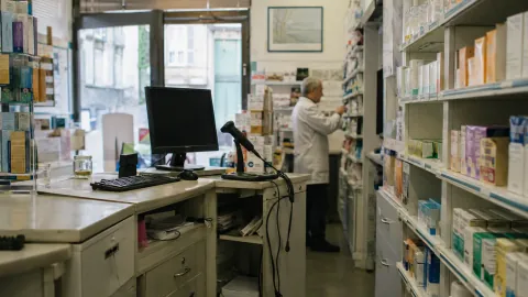 Comptoir et rayonnages d'une pharmacie de quartier, avec un pharmacien en arrière-plan.