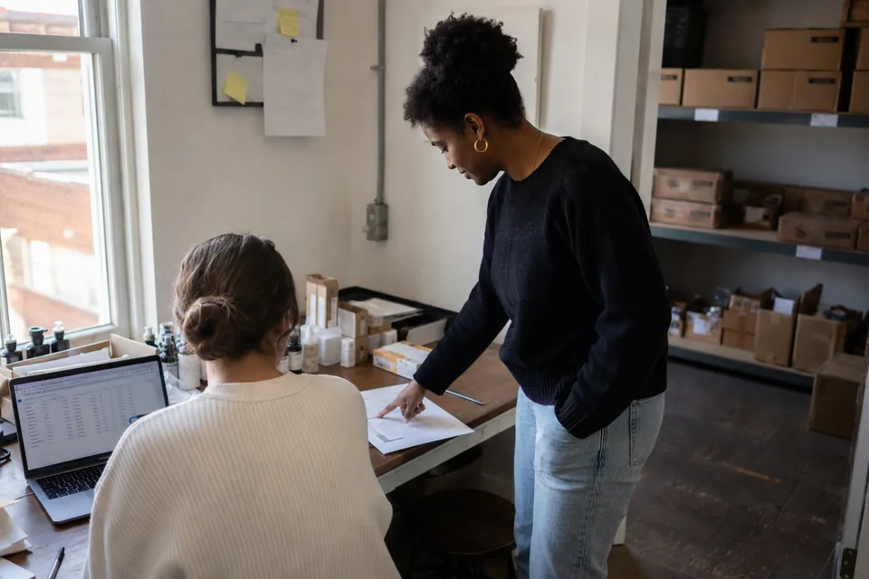 Two colleagues from a small brand study a document beside their stockroom.