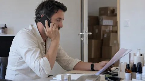 Un responsable de marque téléphone à son bureau en consultant un dossier, près de quelques produits de soin.