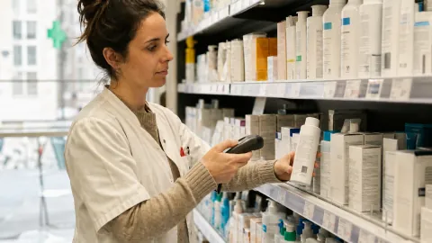 Un pharmacien contrôle les produits d'une étagère avec un lecteur de codes-barres.